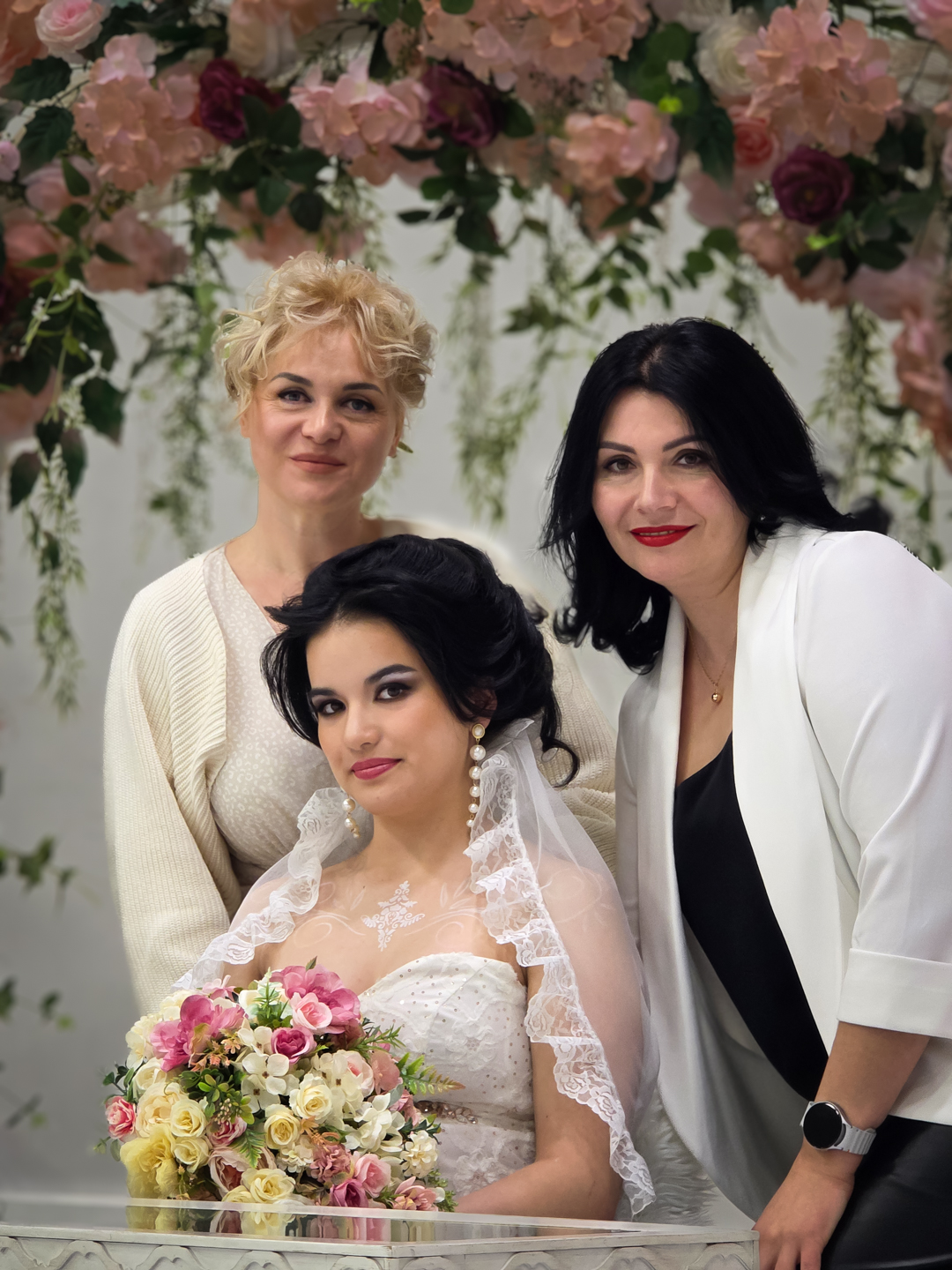 Bride with two women beside a flower arch