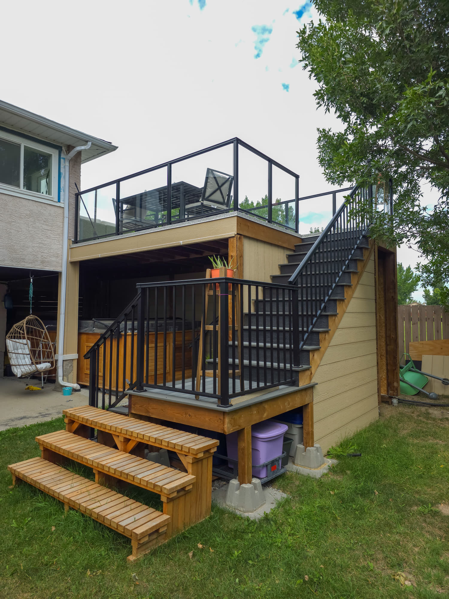 Raised deck with black aluminum railings and glass panels, with a spa tucked underneath